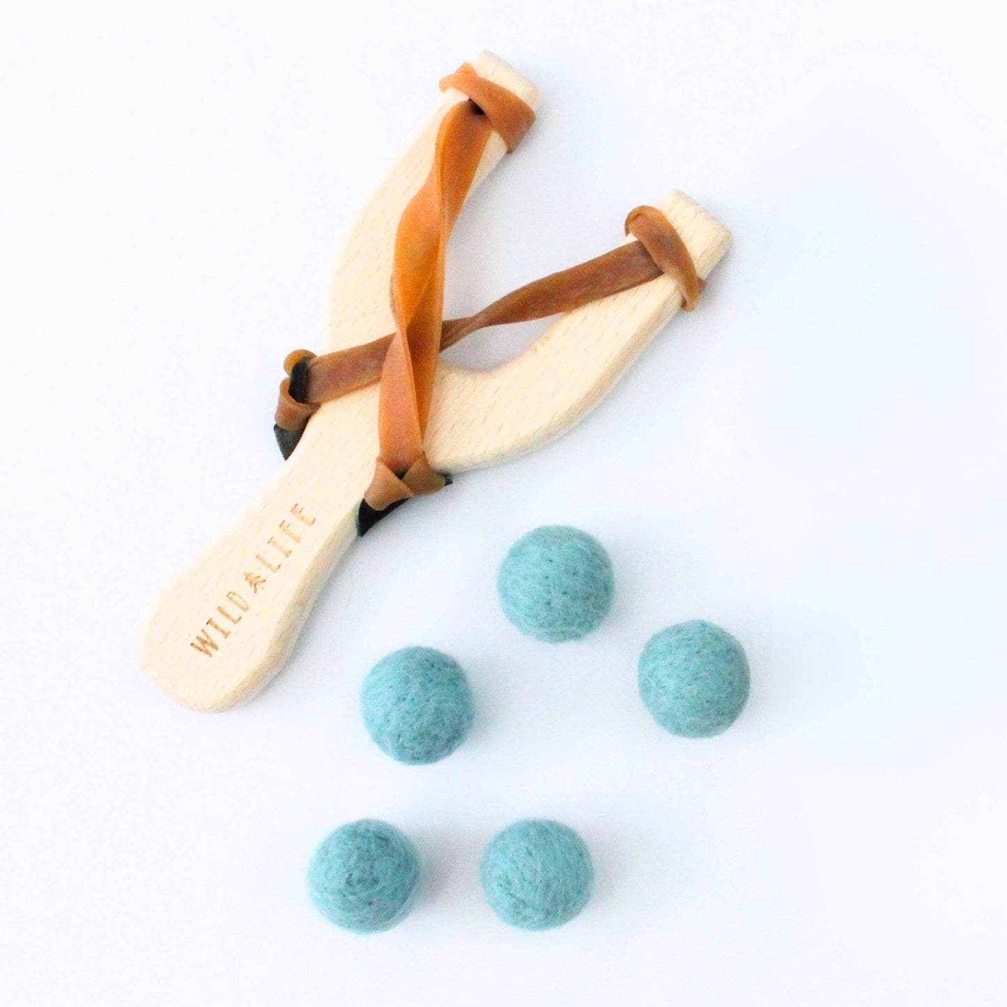 Wooden slingshot with leather straps and blue felt balls on a white background