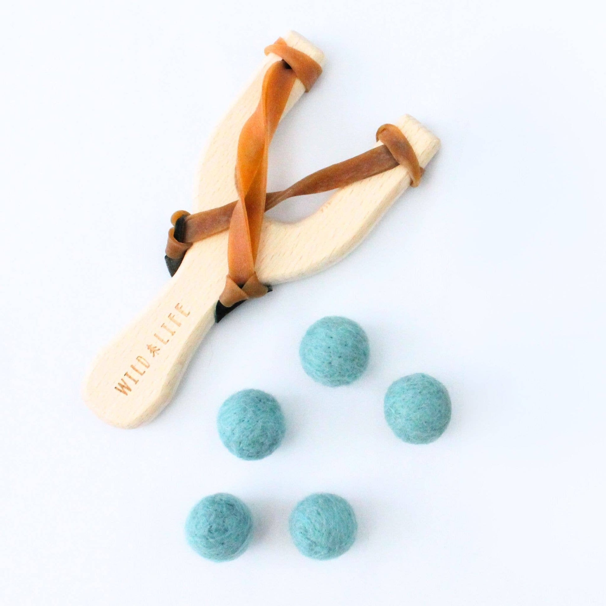 Wooden slingshot with leather straps and blue felt balls on a white background