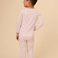 A young boy viewed from the back wearing a long-sleeve pajama set with a small orange and white repeating pattern, set against a solid beige studio background.
