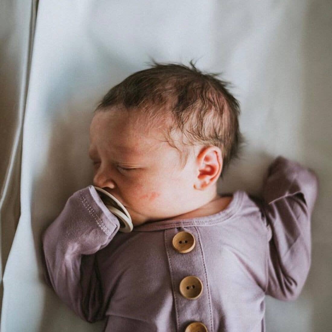 Newborn baby wearing a purple outfit with gold buttons