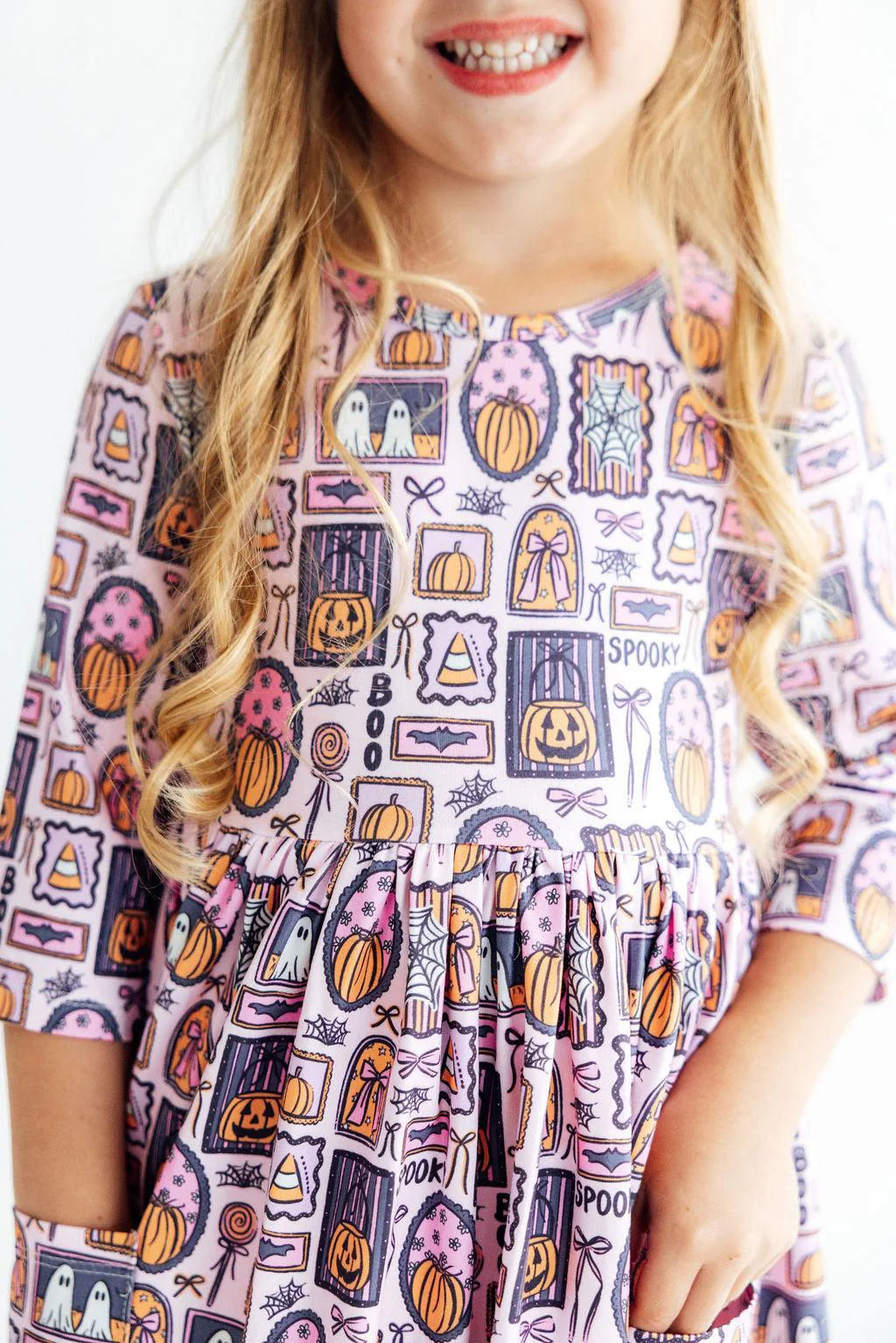 Child wearing a Halloween-themed dress with pumpkins and ghosts on a white background