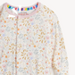 A close-up of a baby long-sleeve top with a colorful pastel floral and leaf print featuring small smiling faces. The garment has a pink collar and a magnetic snap closure at the neckline.