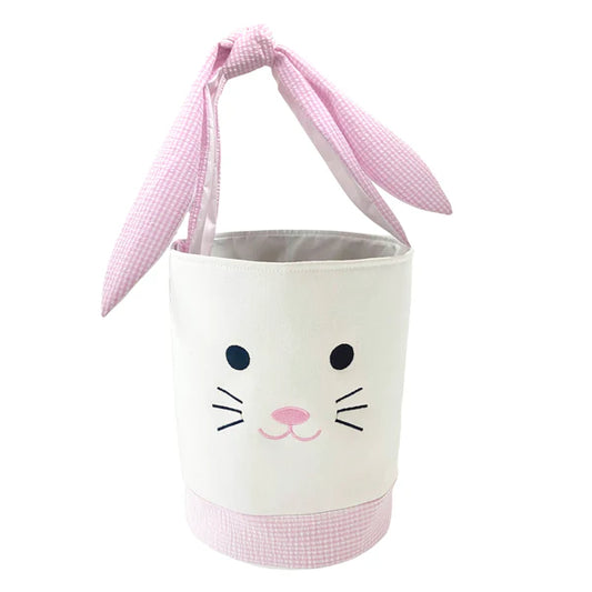 A pink and white bunny-themed basket with bunny ear straps and embroidered bunny face, made from cotton and seersucker.