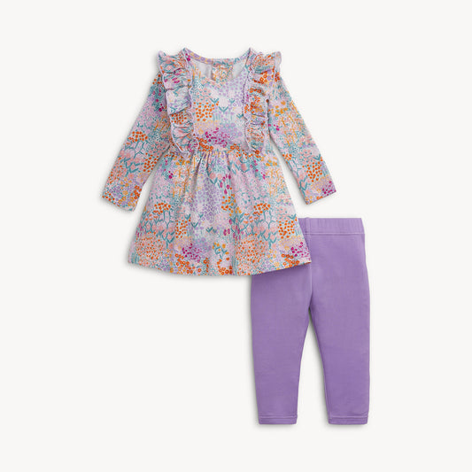 A  girl's two-piece outfit set featuring a long-sleeve ruffle-neck dress with a multicolor floral print and solid purple leggings.